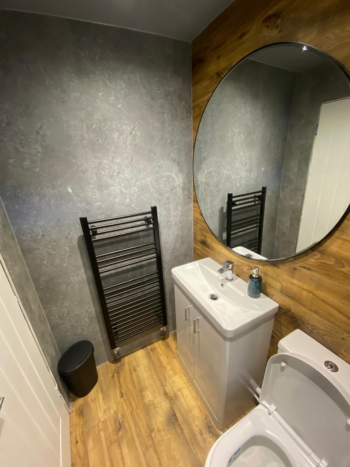 Modern bathroom with a round mirror, oak vanity unit and grey tiling