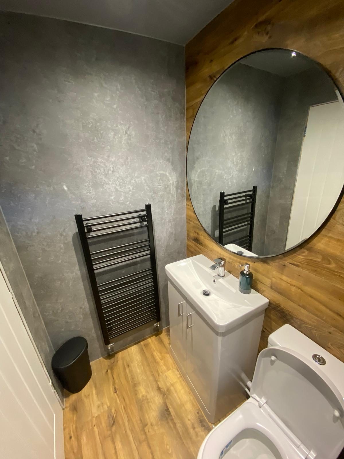 Grey bathroom with a large round mirror and heated towel rail