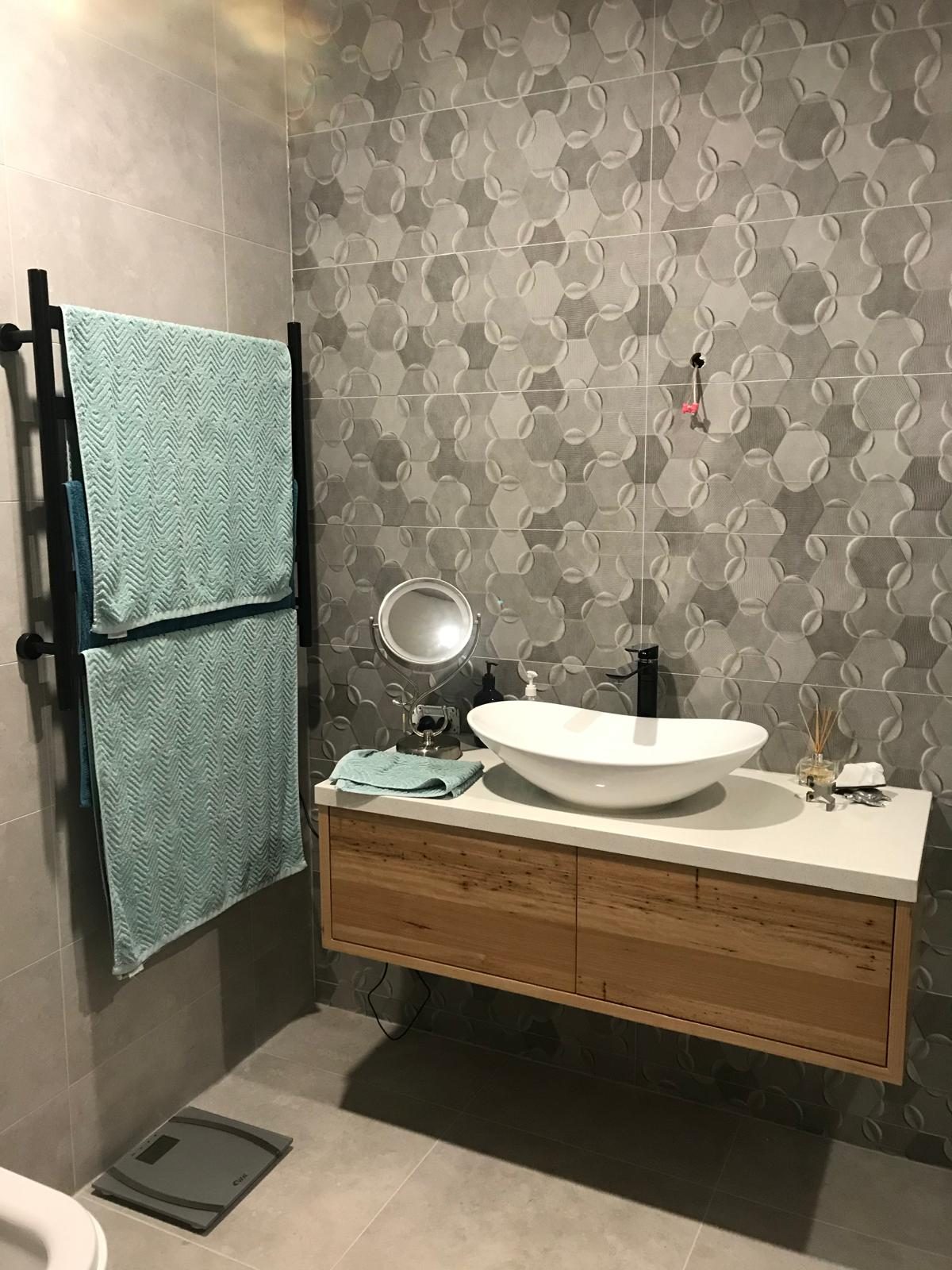 Bathroom with a patterned feature wall, oak vanity and heated towel rail